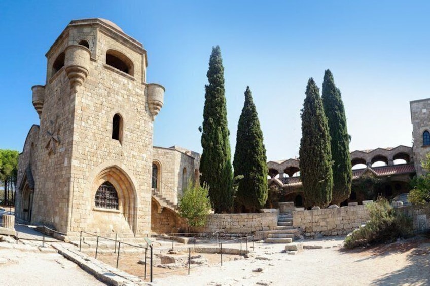 An ancient stone building with a tower, surrounded by cypress trees. 2