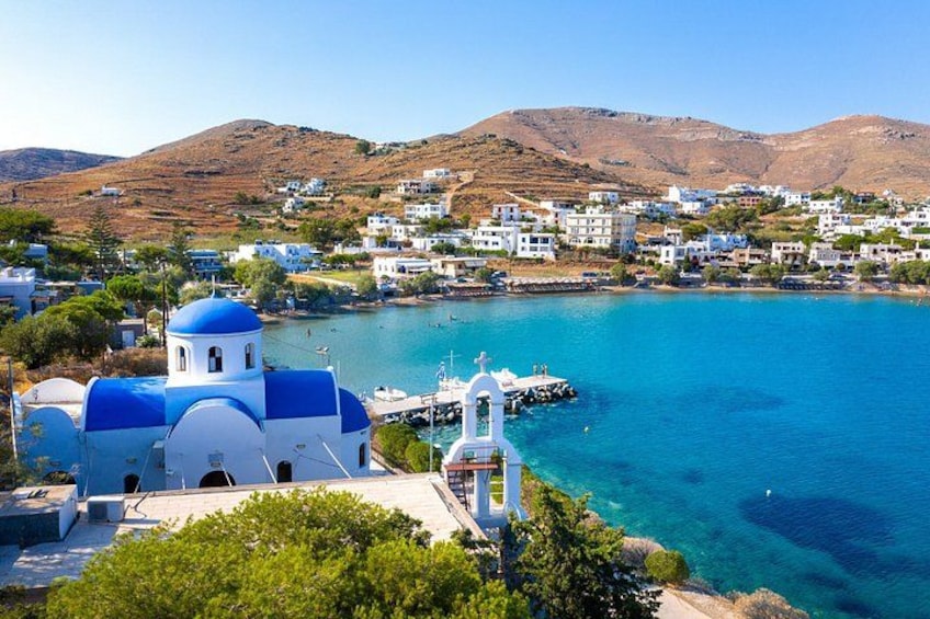 A coastal town with a prominent church, clear blue waters, and hilly terrain in the background. 1