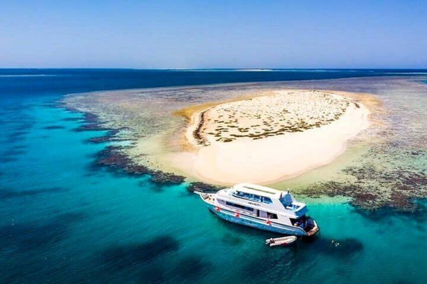 Een boot verankerd nabij een koraalrif, omgeven door turquoise water en een klein eiland. 1