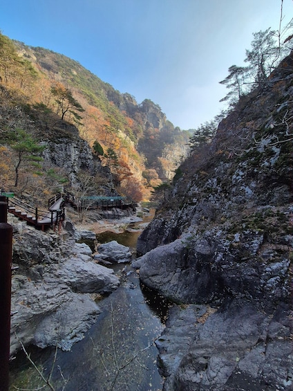 A rocky riverbed with a wooden bridge and a wooden walkway in a mountainous area. 1