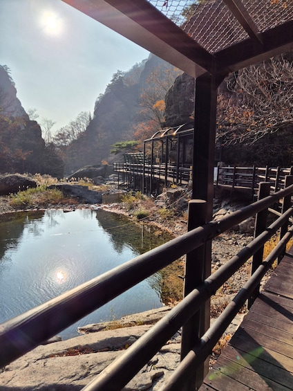 A wooden bridge over a calm river, surrounded by rocky terrain and autumn foliage. 3
