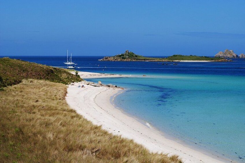 A beach with clear turquoise water, a sandy shore, and a sailboat in the distance. 5