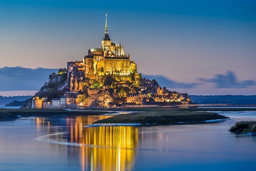 A castle on a rocky island with a calm body of water in the foreground. 2