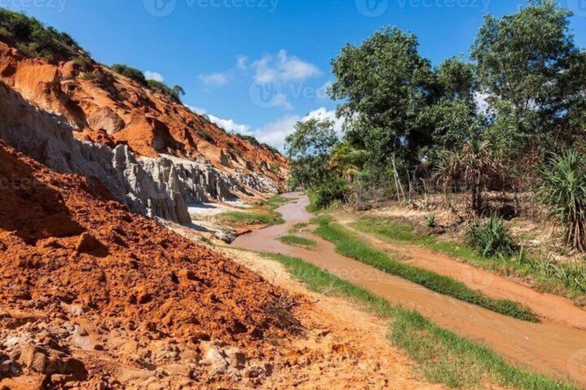 Ein unbefestigter Weg schlängelt sich durch eine hügelige Landschaft mit roter Erde und grüner Vegetation. 3