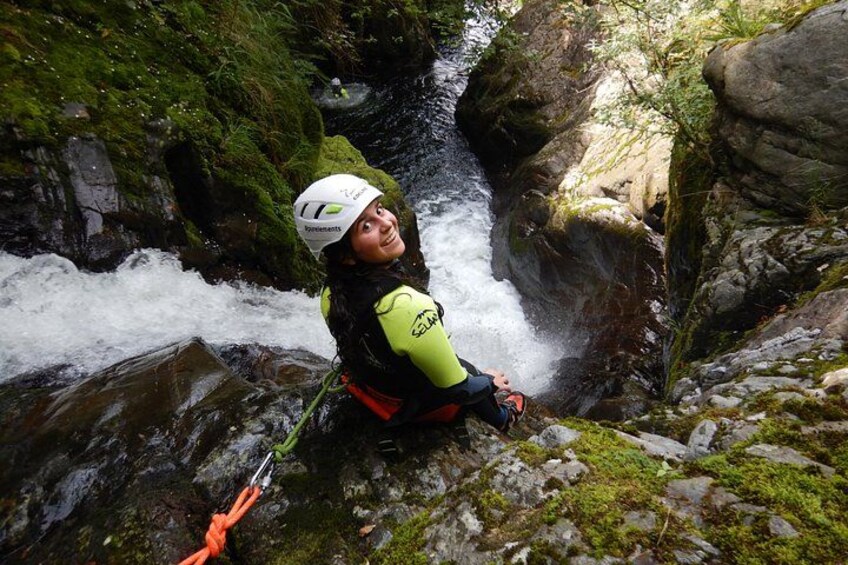 A person in a yellow jacket and helmet near a fast-flowing river with rocks and greenery. 1