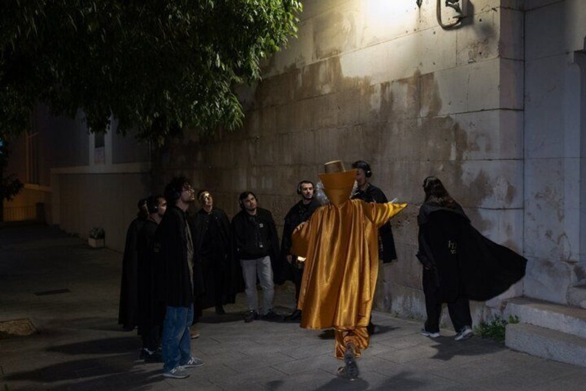 A person in a golden costume standing in a dimly lit alleyway with a group of people. 5