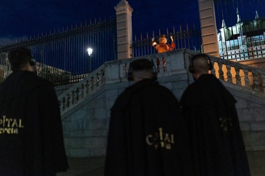 A night scene with a statue on a staircase, a fence, and a building with illuminated windows. 1