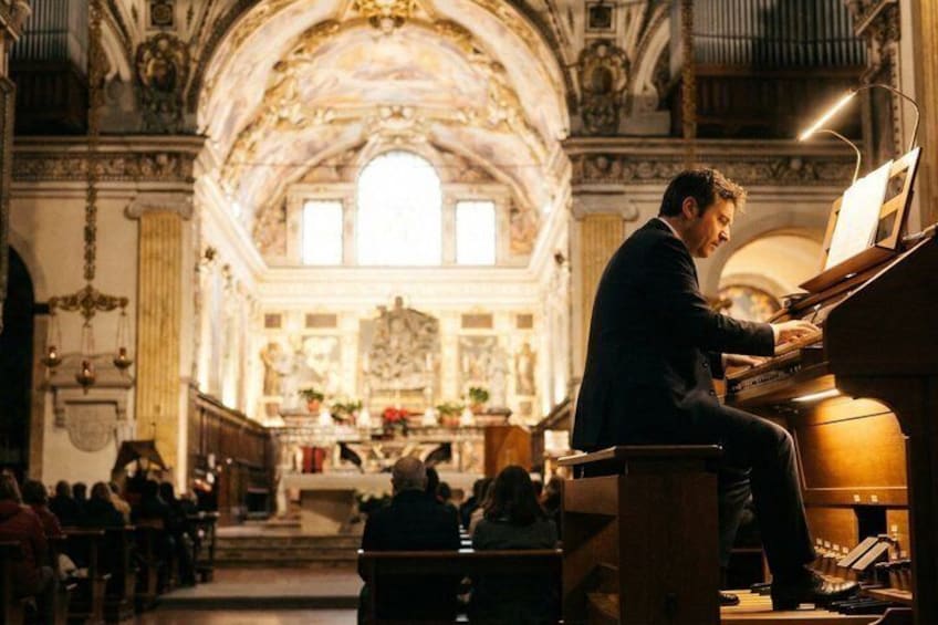 A man playing a grand piano inside a church with ornate architecture and a congregation in the background. 4