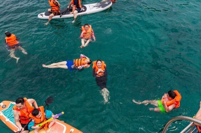 People in the water wearing life jackets, some on paddleboards. 2