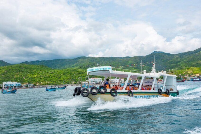 A ferry with multiple decks and passengers, traveling on a body of water with other boats and a mountainous landscape in the background. 1