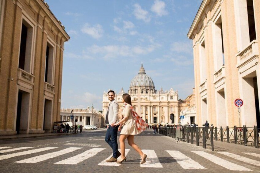 A couple crossing a street with St. Peter's Basilica in the background. 1