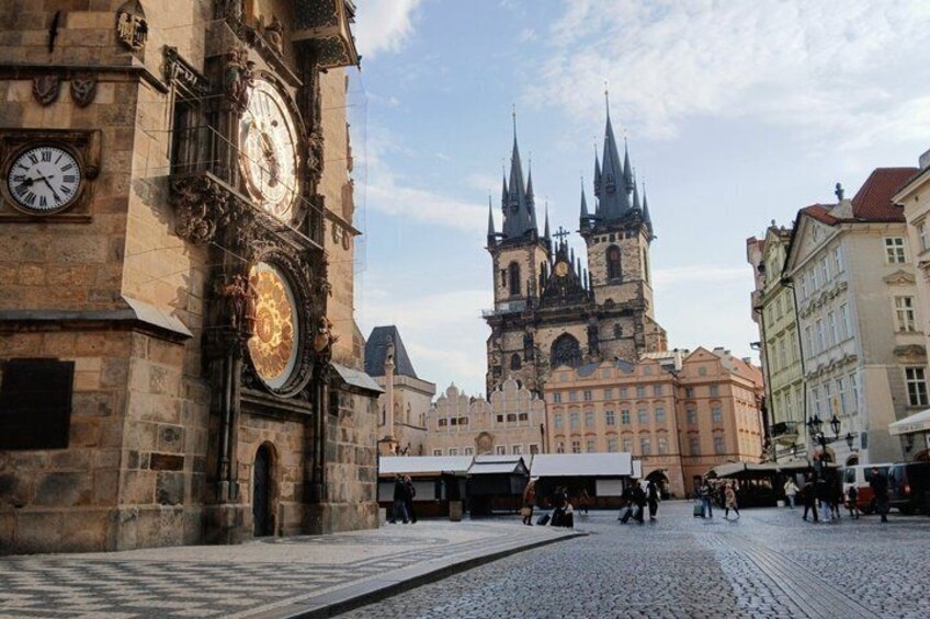A historic square with a prominent clock tower and a church with twin spires in the background. 1