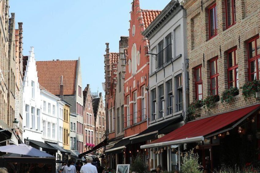 A narrow street lined with historic buildings, some with red awnings and others with white facades. 2
