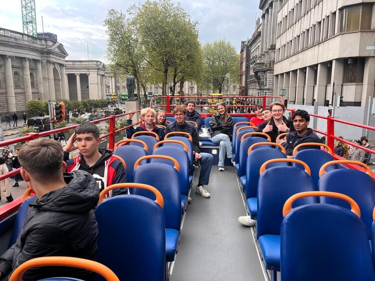 A double-decker bus with passengers seated, surrounded by urban buildings and trees. 2