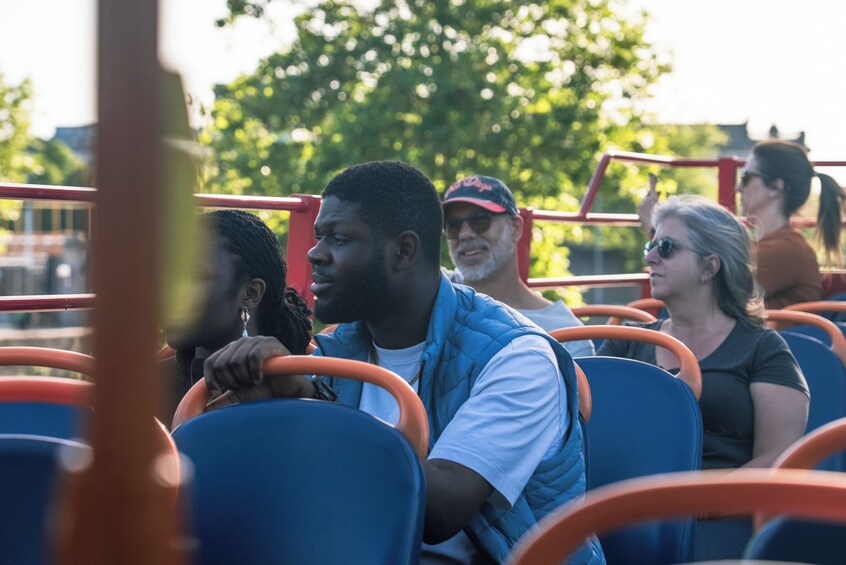 People seated on a bus with blue seats and orange handrails. 4