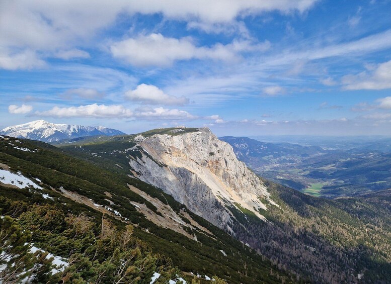 A mountain landscape with a prominent rocky peak, snow-capped mountains in the distance, and a valley below. 1