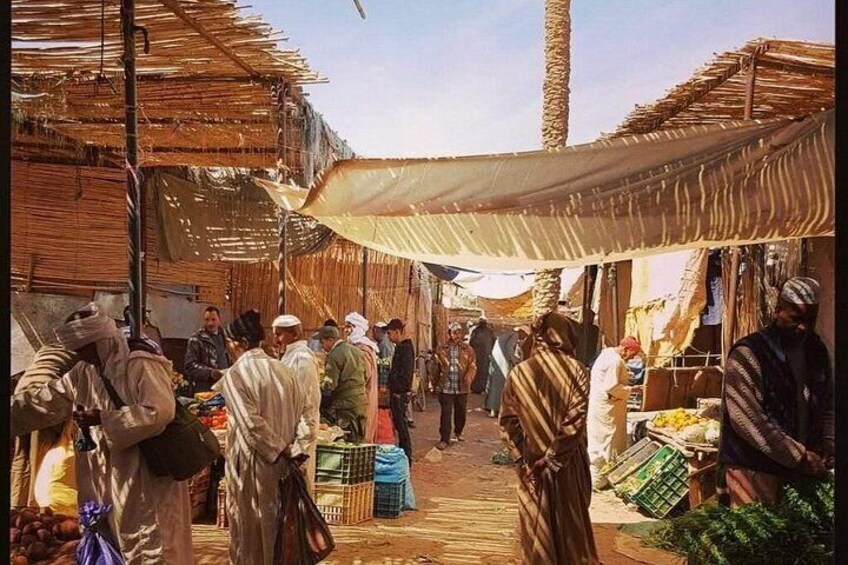 A bustling market with people shopping and vendors selling goods under shaded canopies. 4