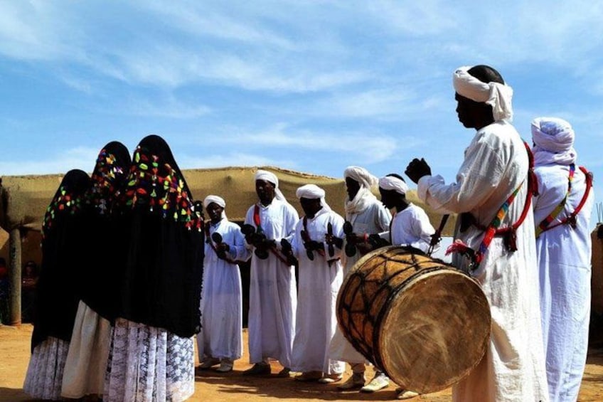 A group of people in traditional attire, some playing drums, in a desert setting. 4