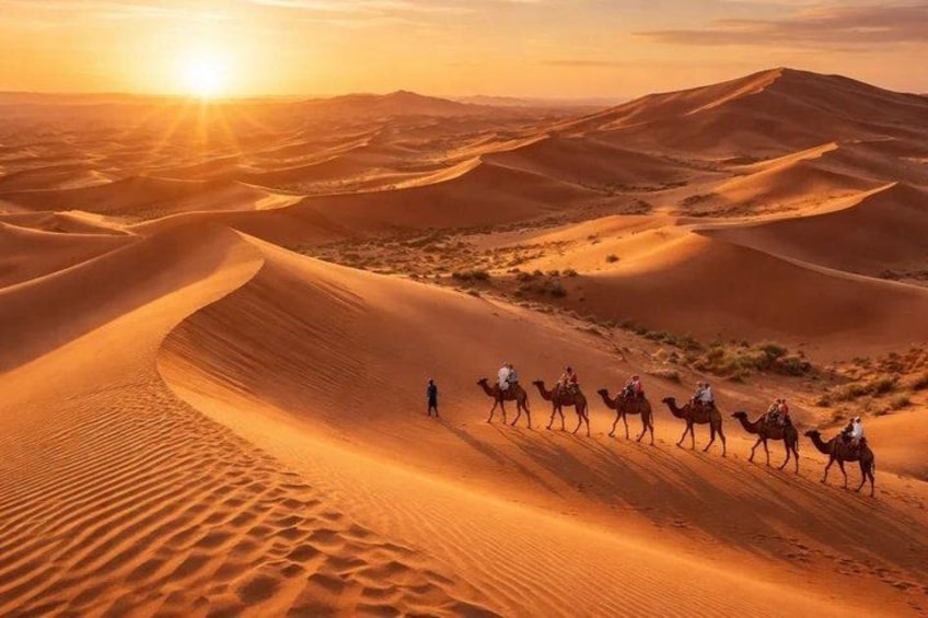 A desert landscape with sand dunes and a group of camels with riders. 2