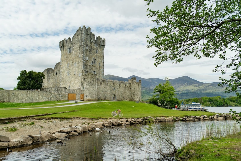 A historic castle with a moat, a bicycle, and a boat on a lake. 4