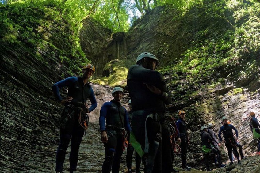 Een groep mensen in een bebost gebied met rotsachtig terrein, uitgerust met helmen en tuigjes, wat erop wijst dat ze aan het klimmen of abseilen zijn. 2