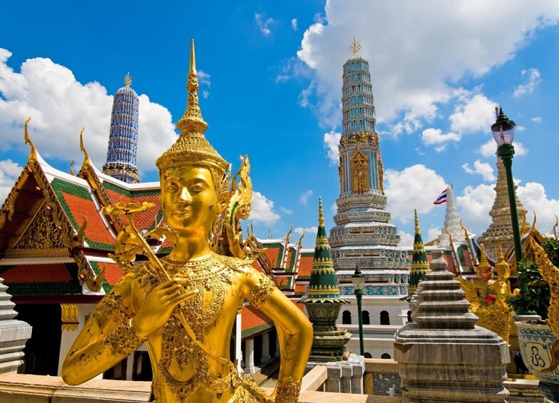 A golden Buddha statue in front of a temple with ornate architecture and a tall spire. 1