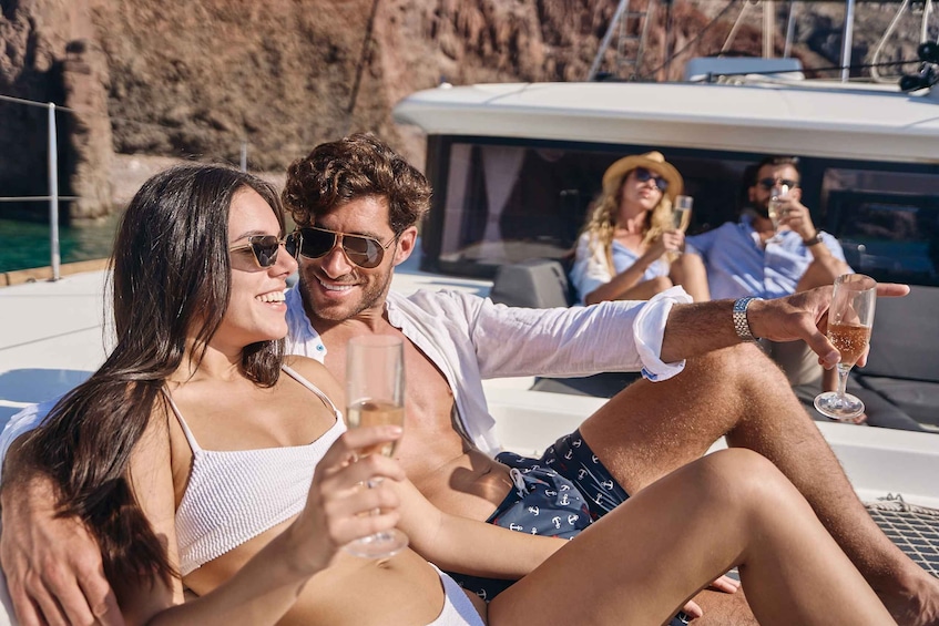 A group of people on a yacht, holding glasses of champagne, with a rocky coastline in the background. 2