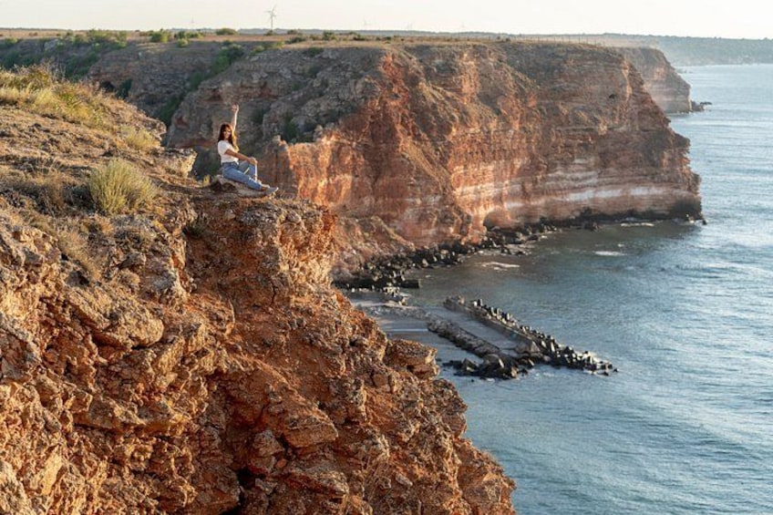A person sitting on a rocky cliff overlooking a coastal area with cliffs and the sea. 1