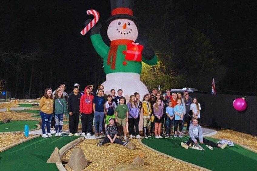 A group of people posing in front of a large snowman decoration. 2