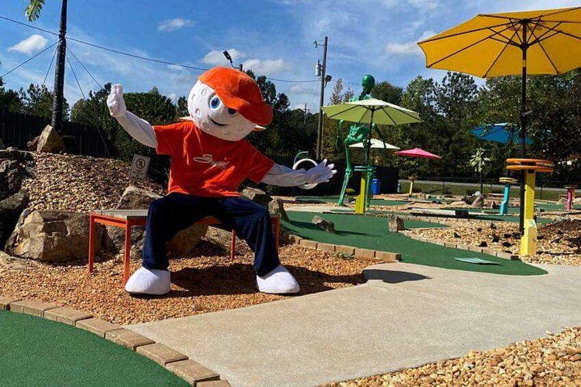 A mascot sitting on a bench, surrounded by playground equipment and umbrellas. 1
