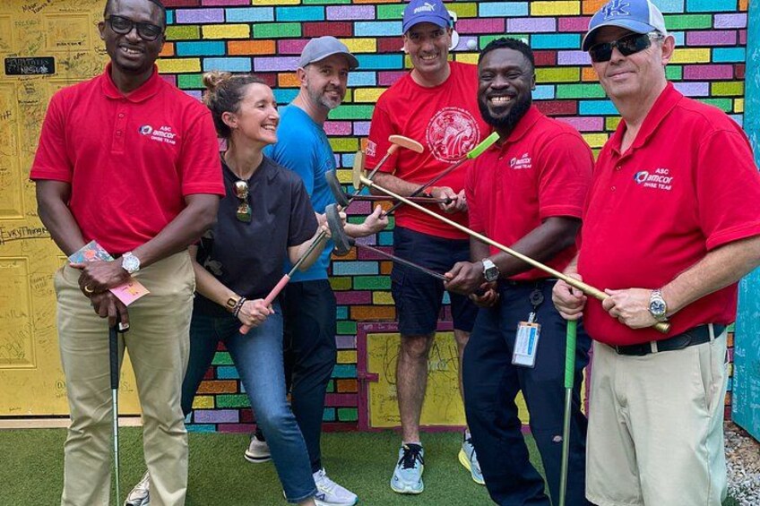 Un groupe de personnes portant des chemises rouges et tenant des clubs de golf devant un mur de briques aux couleurs vives. 2