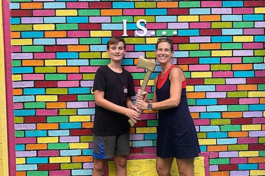 Two people holding a trophy in front of a colorful brick wall. 2