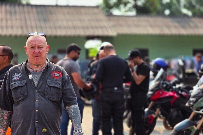 A man with tattoos and a motorcycle in a group setting. 5