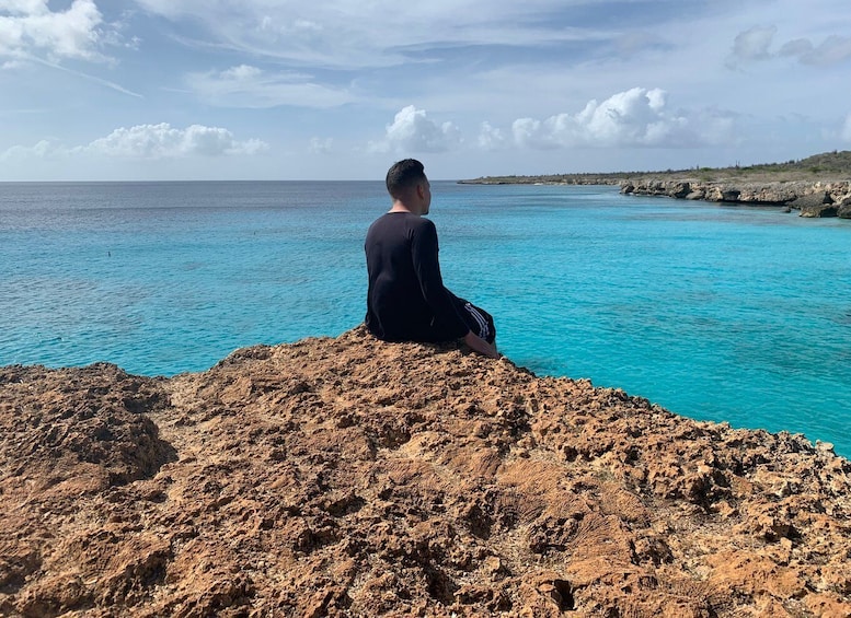 A person sitting on a rocky outcrop overlooking a turquoise sea. 5