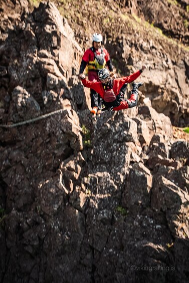 A person in red gear performing a jump on a rope bridge over rocky terrain. 4