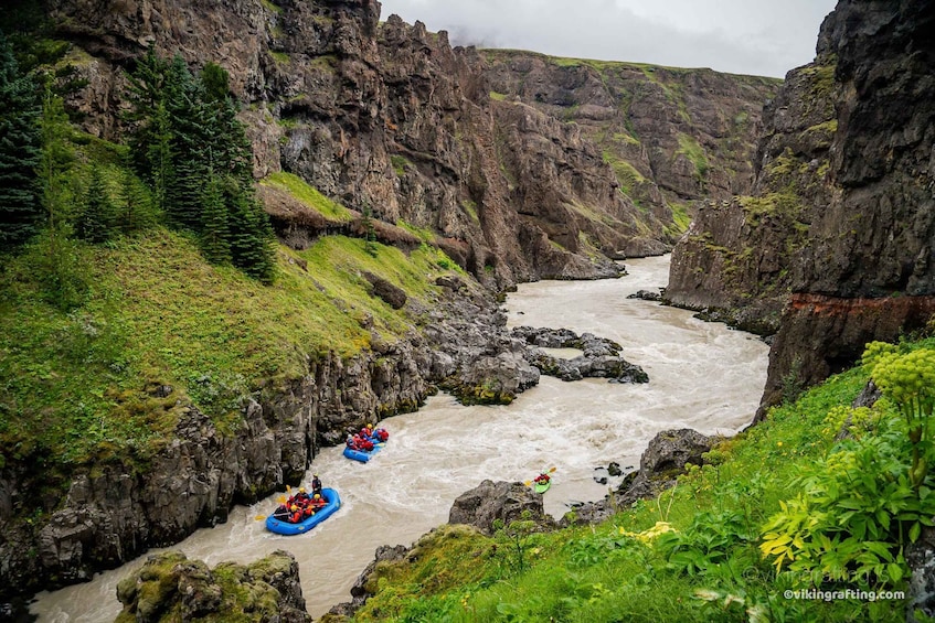 A river canyon with kayaks and a blue raft navigating the waters. 1