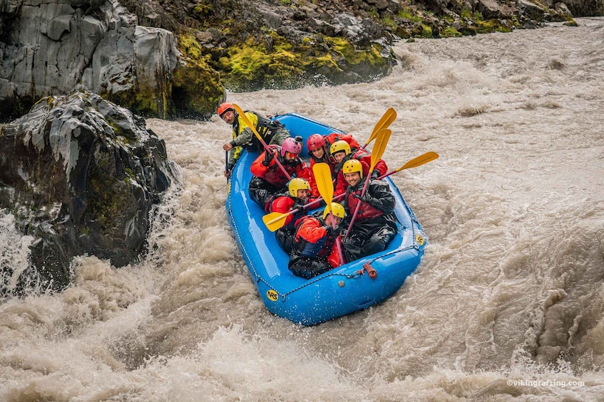 A group of people in a blue inflatable raft navigating a turbulent river. 1