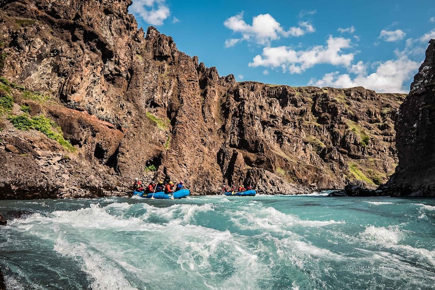 A group of people rafting on a river with rocky cliffs in the background. 5