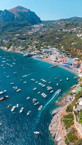 A coastal town with a marina filled with boats, a beach with umbrellas, and a mountainous backdrop. 3