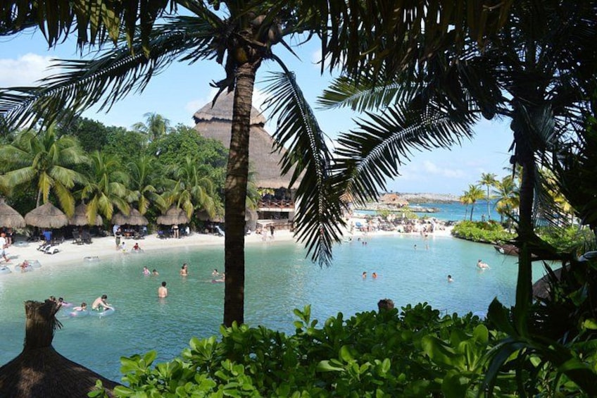 Een tropisch strand met palmbomen, een zwembad en een uitzicht op een resort in de verte. 2
