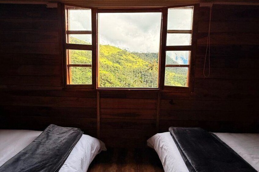 A cabin with two beds, a large window, and a view of a green landscape. 5