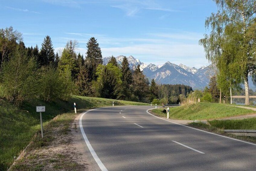 A winding road with a mountain backdrop, clear skies, and lush greenery. 4