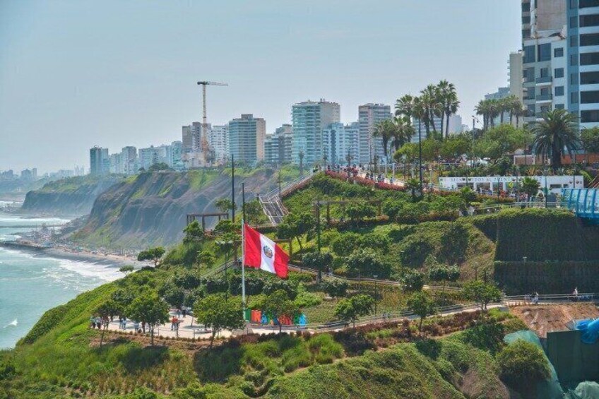 A coastal cityscape with a prominent flag, lush greenery, and a clear view of the ocean. 1