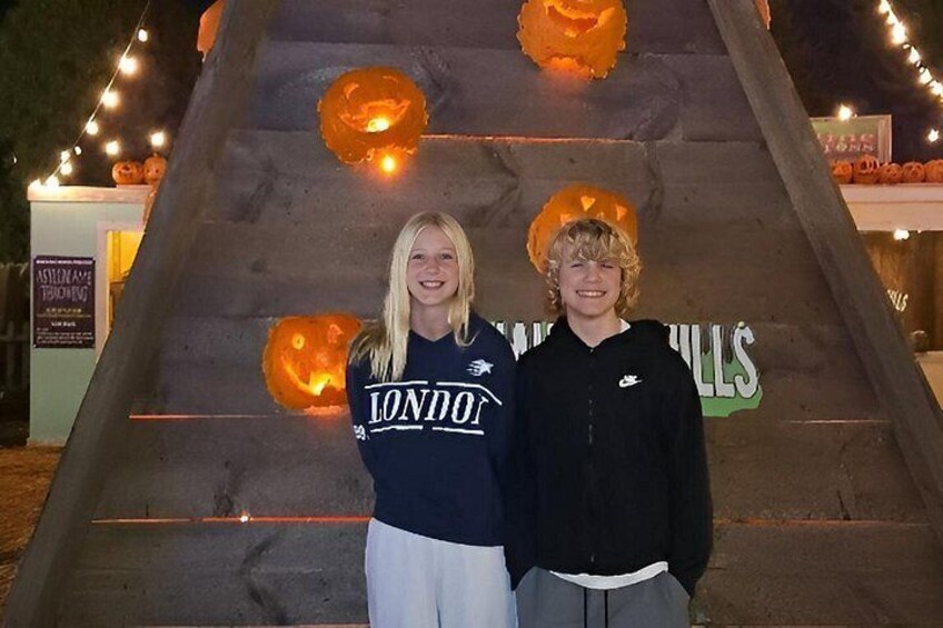 Two people standing in front of a large pumpkin with a sign in the background. 2