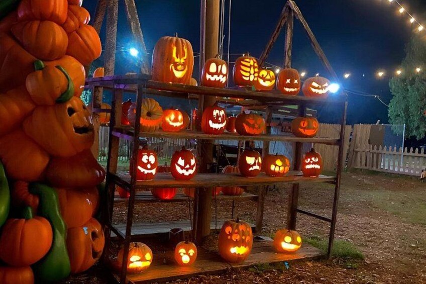 A display of carved pumpkins with various faces, arranged on a wooden stand outdoors at night. 1