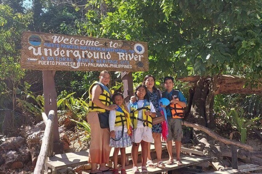 Un groupe de personnes portant des gilets de sauvetage se tient devant un panneau accueillant les visiteurs du fleuve souterrain de Puerto Princesa, à Palawan, aux Philippines. 3