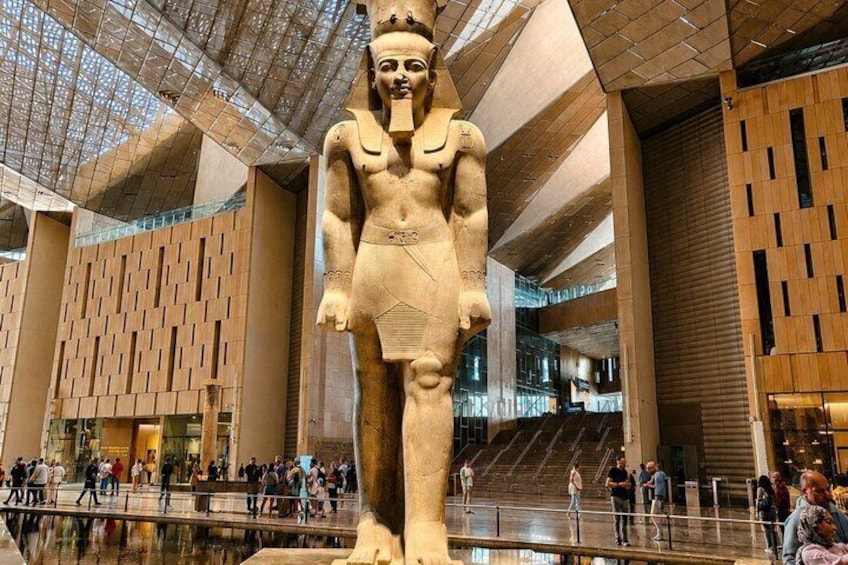 En stor, forntida egyptisk staty i en modern byggnad med högt i tak och väggar med ett mönster. 3