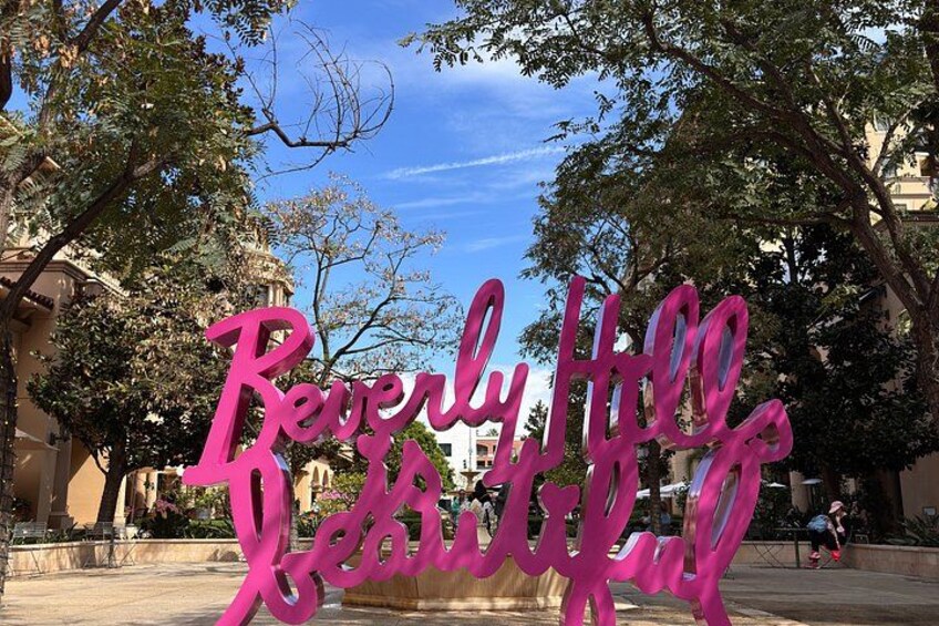 Une pancarte rose sur laquelle on peut lire « Résidences de Beverly Hills », placée sur une place publique, avec des arbres et des bâtiments en arrière-plan. 2