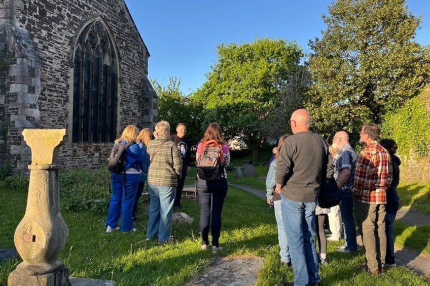 A group of people standing in front of a stone church with a large arched window. 4