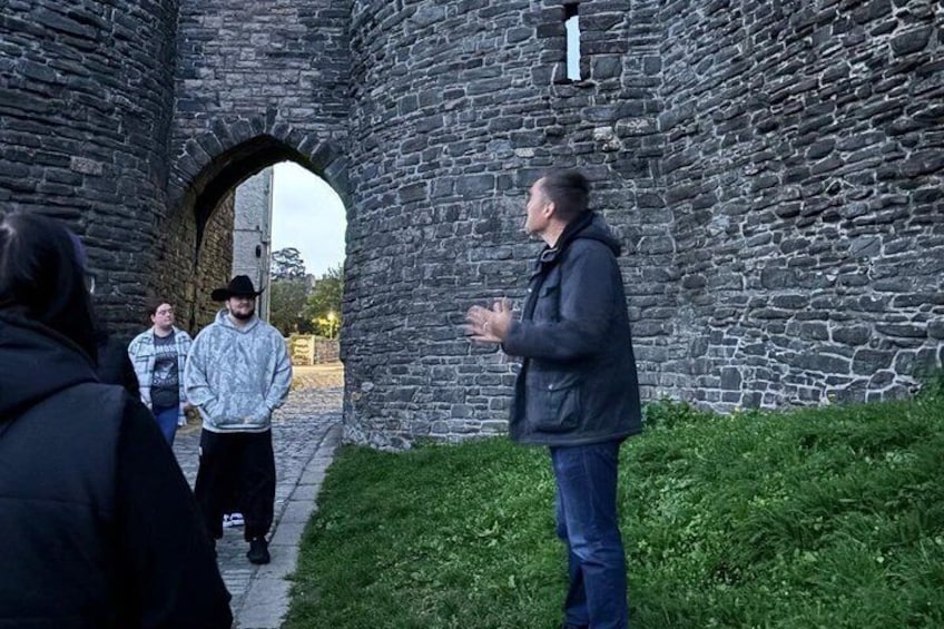 A stone archway, a person gesturing, and a group of people in a historical setting. 5
